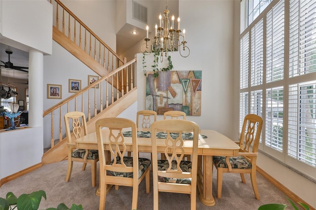 carpeted dining space featuring a towering ceiling, stairway, a chandelier, baseboards, and a ceiling fan