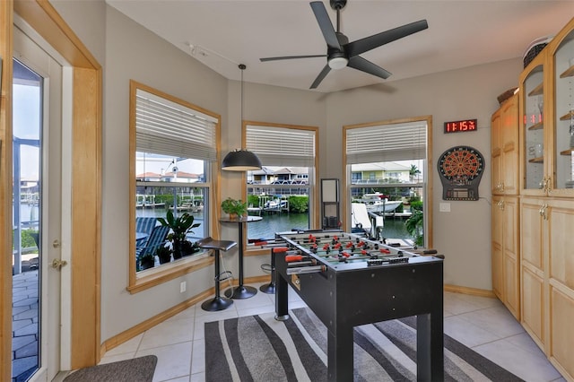 rec room with ceiling fan, light tile patterned floors, a water view, and baseboards
