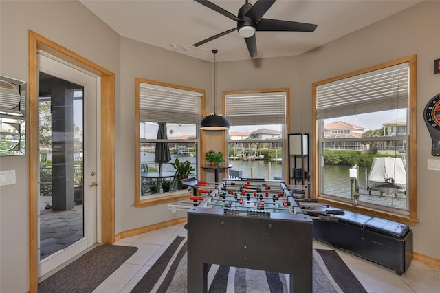 game room featuring a ceiling fan, tile patterned floors, a water view, and baseboards