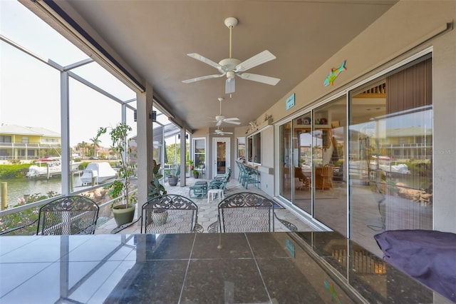unfurnished sunroom featuring a ceiling fan, a water view, and outdoor dining space