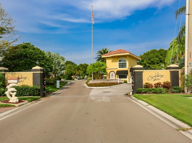 view of asphalt street with curbs, a gated entry, and street lights