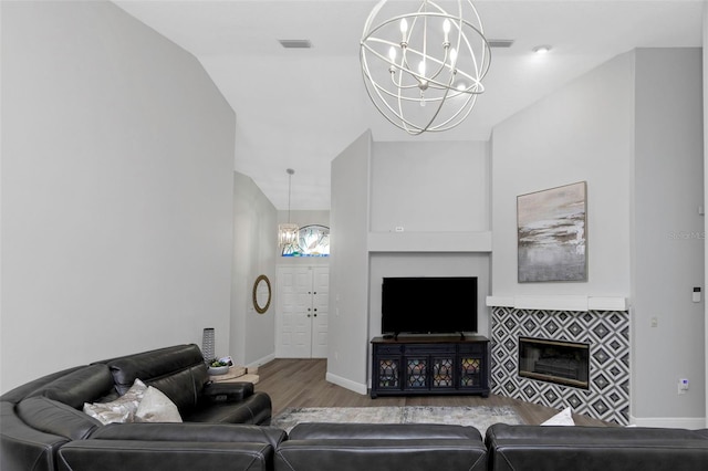 living area featuring a chandelier, wood finished floors, a tile fireplace, and baseboards