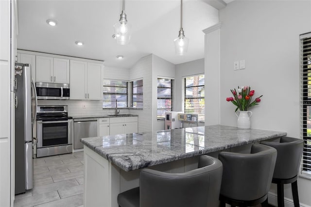 kitchen with appliances with stainless steel finishes, a sink, a peninsula, a breakfast bar, and vaulted ceiling