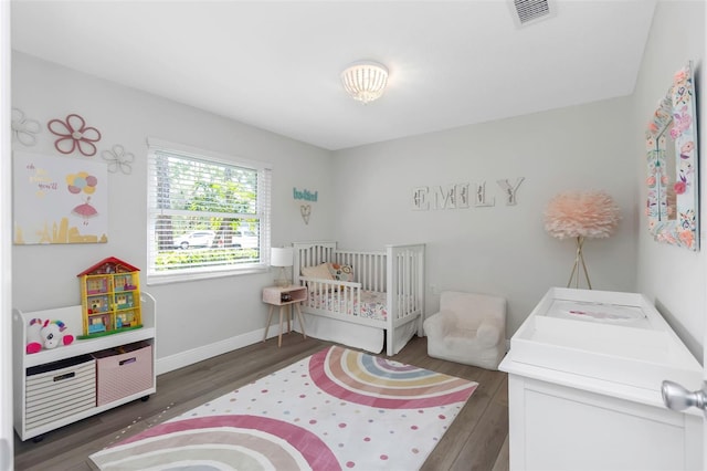 bedroom with wood finished floors, a crib, and baseboards