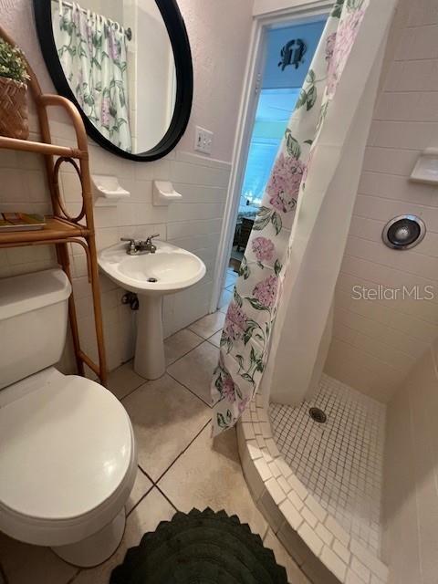 3031 56th St S, Gulfport, FL 33707 - bathroom with tile walls, a stall shower, toilet, tile patterned floors, and wainscoting