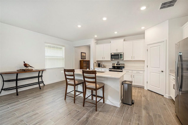 10098 Banyan Breeze Blvd, Land O Lakes, FL 34638 - kitchen featuring appliances with stainless steel finishes, light wood-type flooring, baseboards, light countertops, and an island with sink