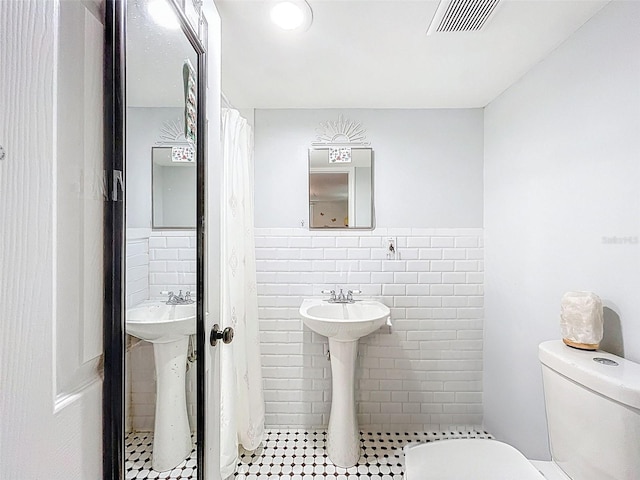 1221 E Hamilton Ave, Tampa, FL 33604 - bathroom with tile walls, toilet, tile patterned floors, wainscoting, and a sink