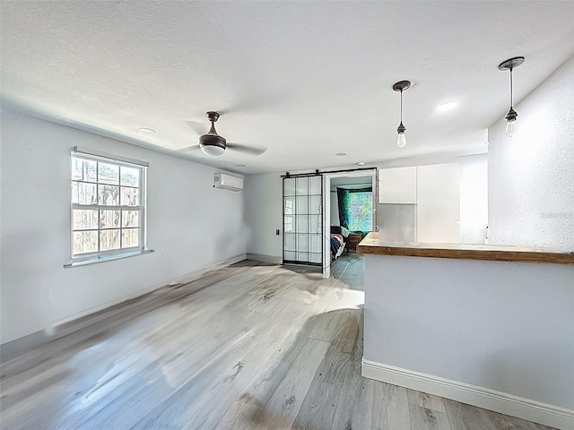 1221 E Hamilton Ave, Tampa, FL 33604 - unfurnished living room with light wood-type flooring, baseboards, a wall unit AC, a barn door, and healthy amount of natural light