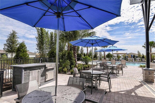 view of patio / terrace with outdoor dining space, exterior kitchen, a community pool, a sink, and fence