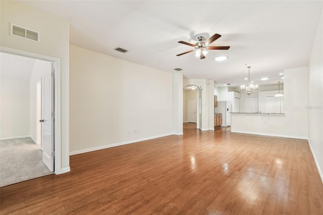 unfurnished living room with ceiling fan, a chandelier, light wood-style floors, and baseboards