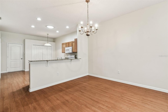 kitchen featuring white microwave, wood finished floors, baseboards, recessed lighting, and range