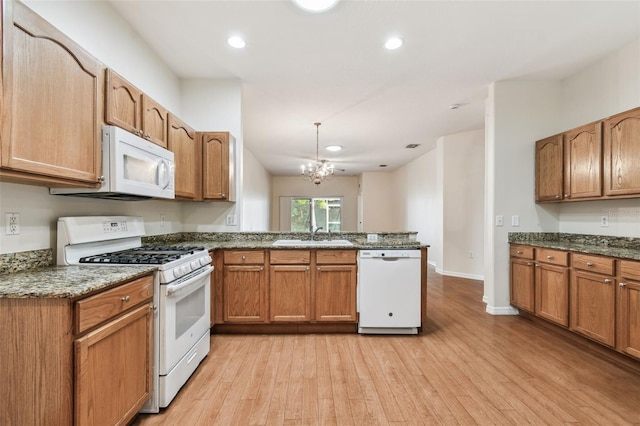 kitchen with white appliances, a peninsula, light wood-style flooring, a sink, and a chandelier