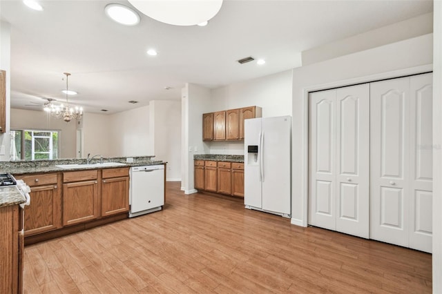 kitchen with white appliances, a sink, brown cabinets, a peninsula, and hanging light fixtures