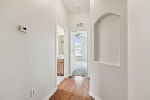 corridor with light wood-type flooring, baseboards, and a sink