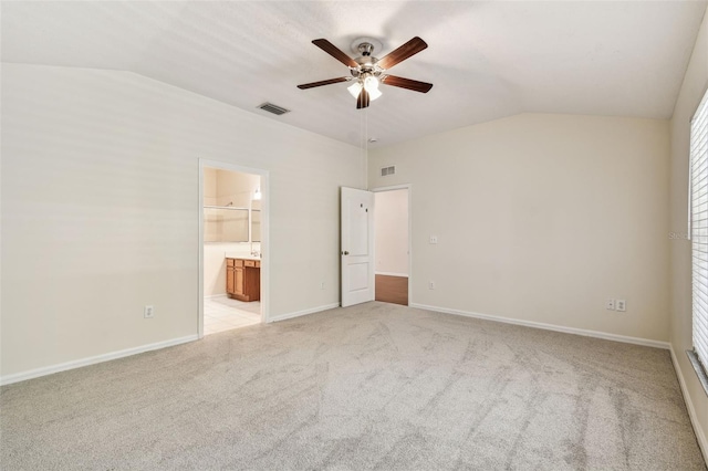 unfurnished bedroom with vaulted ceiling, light colored carpet, ensuite bath, baseboards, and ceiling fan
