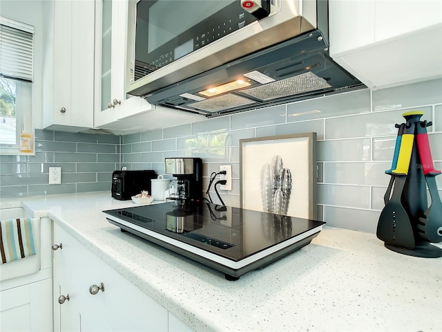 5111 28th Ave N, Saint Petersburg, FL 33710 - kitchen featuring stainless steel microwave, white cabinets, backsplash, black electric stovetop, and light stone countertops