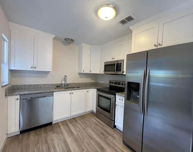 5111 28th Ave N, Saint Petersburg, FL 33710 - kitchen featuring appliances with stainless steel finishes, a sink, light wood-type flooring, white cabinets, and dark stone countertops