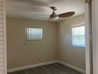 spare room featuring a ceiling fan, baseboards, and dark wood-style floors