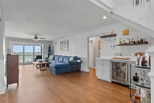 297 1st St W, Tierra Verde, FL 33715 - living room with wine cooler, a bar, a ceiling fan, a textured ceiling, and light wood-style floors