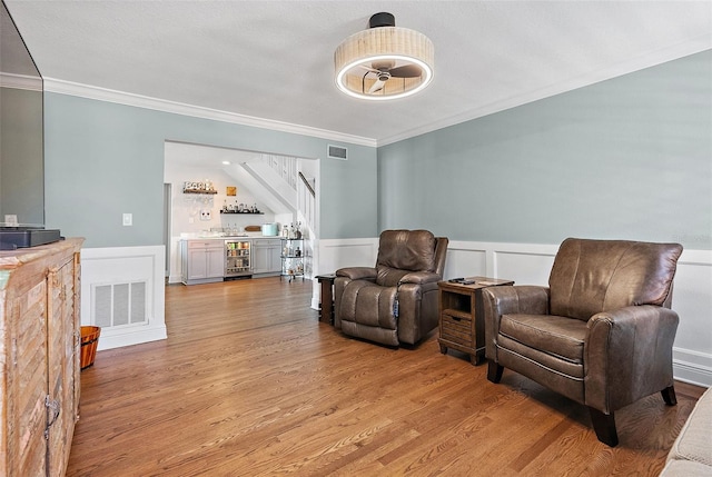 297 1st St W, Tierra Verde, FL 33715 - sitting room with beverage cooler, a bar, crown molding, wainscoting, and light wood-style floors