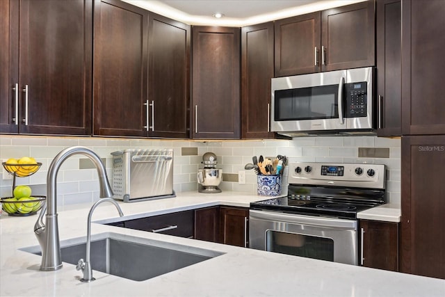 2626 2nd Ct, Palm Harbor, FL 34684 - kitchen featuring appliances with stainless steel finishes, a sink, tasteful backsplash, dark brown cabinets, and light stone counters