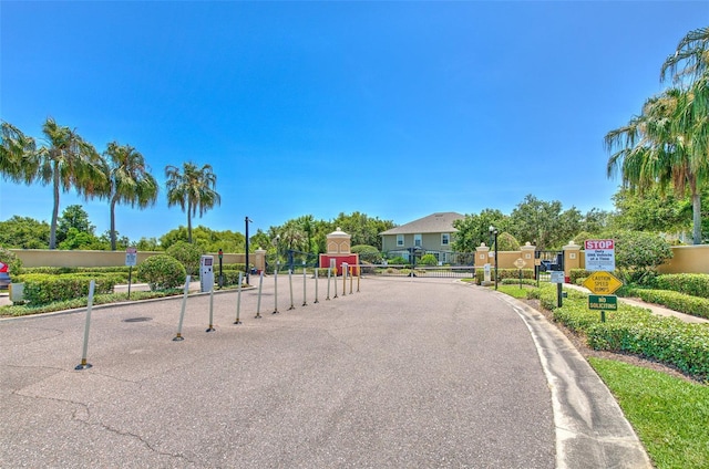 view of asphalt road with traffic signs, street lights, a gated entry, and curbs
