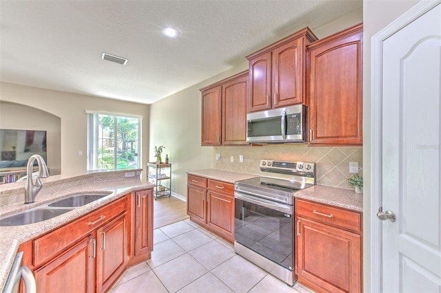 kitchen featuring appliances with stainless steel finishes, a sink, tasteful backsplash, light tile patterned floors, and light stone counters