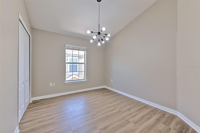unfurnished room with a chandelier, light wood-style flooring, baseboards, and vaulted ceiling
