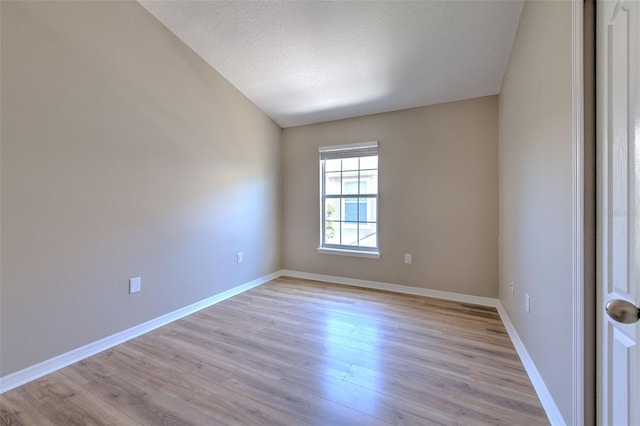 spare room featuring light wood-type flooring, baseboards, and a textured ceiling
