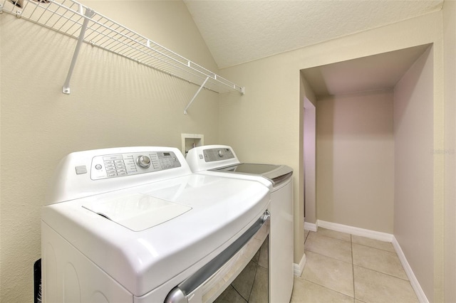 laundry area with washing machine and clothes dryer, light tile patterned flooring, a textured ceiling, and baseboards