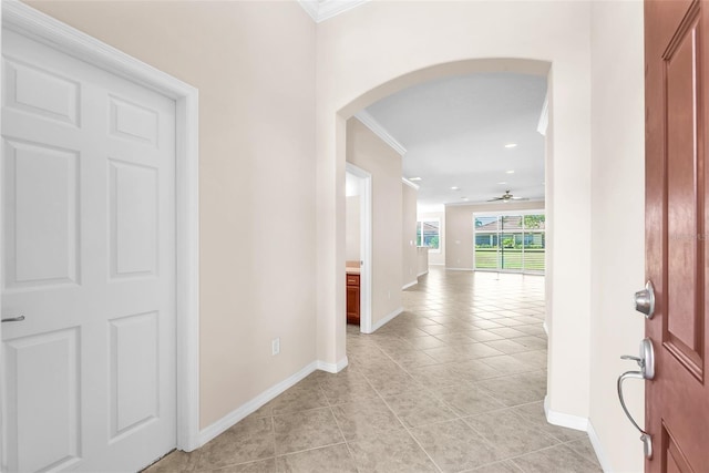 entrance foyer featuring arched walkways, crown molding, light tile patterned floors, ceiling fan, and baseboards