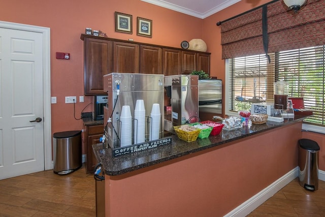 kitchen with ornamental molding, dark stone countertops, wood finished floors, a peninsula, and baseboards