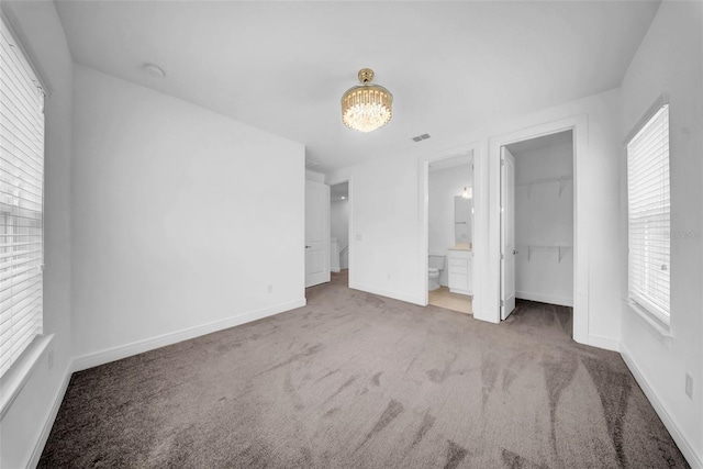 unfurnished bedroom with carpet, a chandelier, baseboards, a spacious closet, and connected bathroom