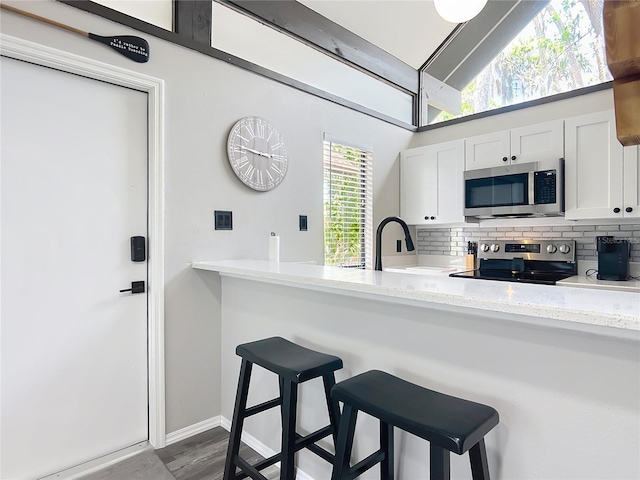 2653 N Seabreeze Pt Unit M-2, Crystal River, FL 34429 - kitchen with appliances with stainless steel finishes, backsplash, white cabinets, a breakfast bar, and lofted ceiling