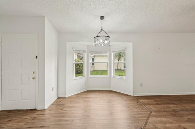 unfurnished dining area with wood finished floors, a chandelier, a textured ceiling, and baseboards
