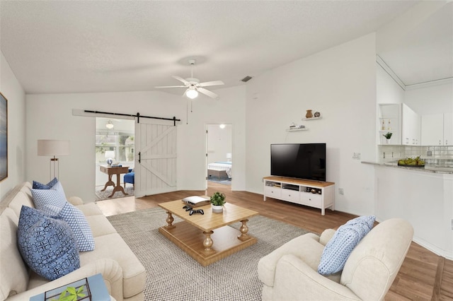 living area with vaulted ceiling, a barn door, ceiling fan, and wood finished floors