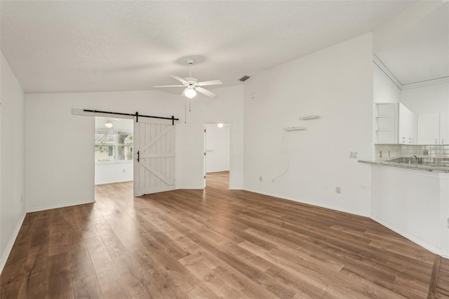 unfurnished living room with lofted ceiling, a barn door, a ceiling fan, light wood-type flooring, and a textured ceiling