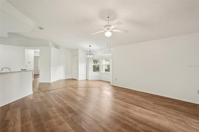spare room featuring a ceiling fan, a textured ceiling, wood finished floors, a chandelier, and baseboards