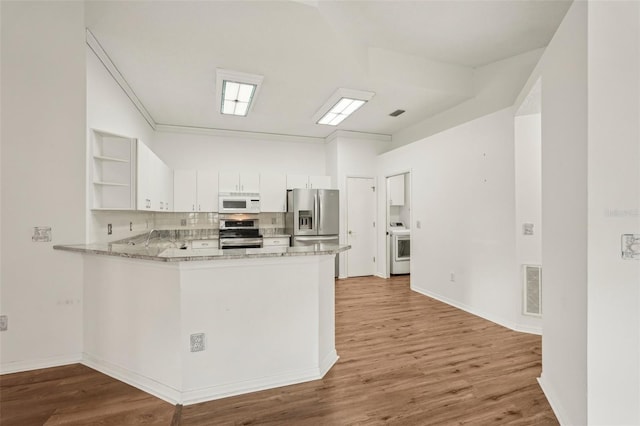 kitchen featuring stainless steel appliances, open shelves, washer / dryer, light wood finished floors, and a peninsula