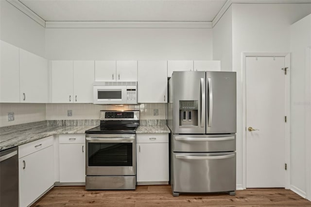 kitchen with stainless steel appliances, ornamental molding, white cabinetry, decorative backsplash, and wood finished floors