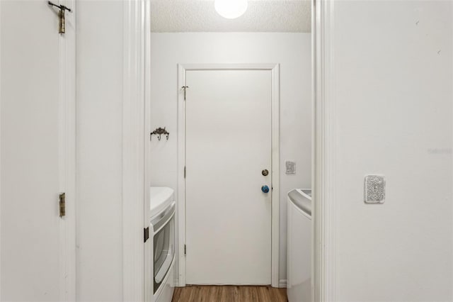 laundry room with washing machine and clothes dryer, a textured ceiling, and light wood-style flooring