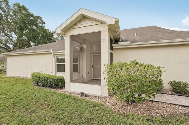 property entrance with a shingled roof, a lawn, and stucco siding