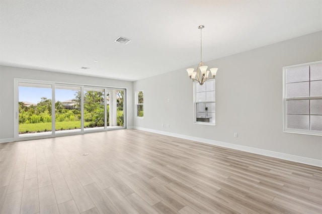 spare room with baseboards, a chandelier, and light wood-style floors