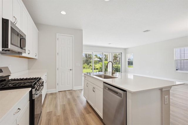 kitchen with appliances with stainless steel finishes, a sink, light wood-style flooring, an island with sink, and light countertops
