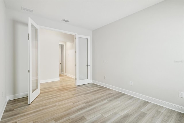empty room with french doors, light wood-style floors, and baseboards