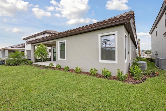 back of house featuring central AC, stucco siding, a yard, and a tile roof