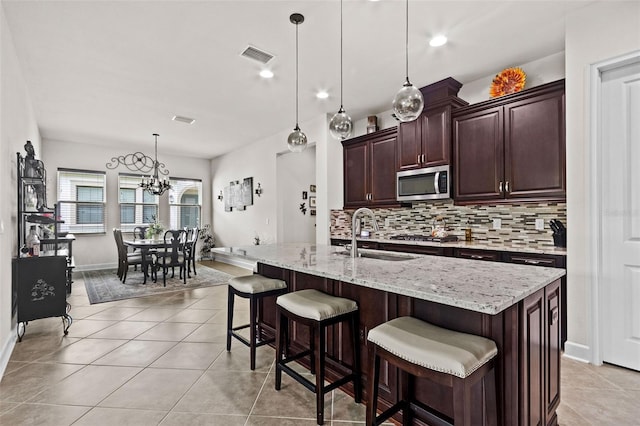 4195 Barletta Ct, Wesley Chapel, FL 33543 - kitchen with stainless steel microwave, tasteful backsplash, a chandelier, dark brown cabinets, and a breakfast bar