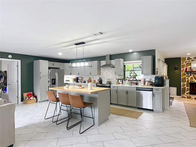 kitchen featuring appliances with stainless steel finishes, wall chimney exhaust hood, gray cabinetry, a breakfast bar area, and tasteful backsplash