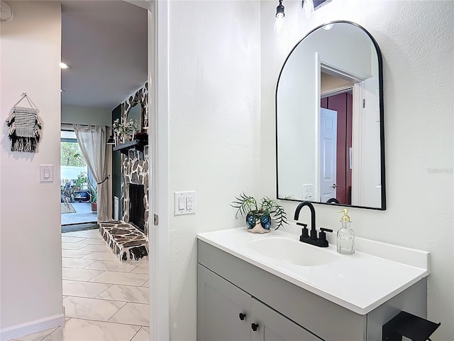 bathroom featuring marble look tiles, vanity, a stone fireplace, and baseboards