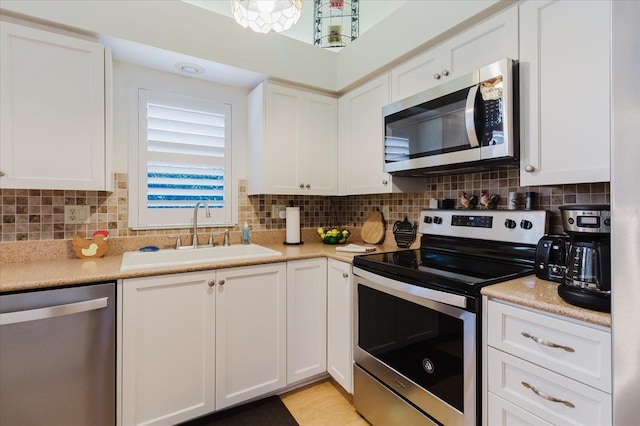 kitchen with stainless steel appliances, a sink, white cabinetry, light countertops, and backsplash